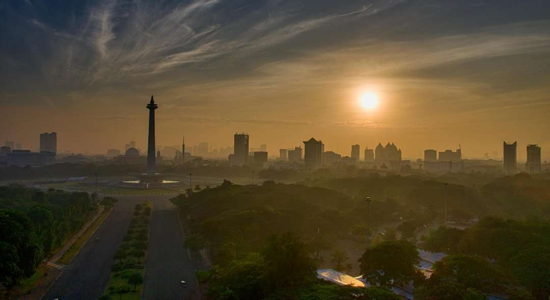A breathtaking aerial view of Jakarta's skyline at sunset, highlighting the iconic National Monument.
