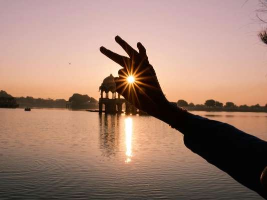 Hand silhouette with sunrays over Indian lake at sunset, creating a peaceful and artistic view.