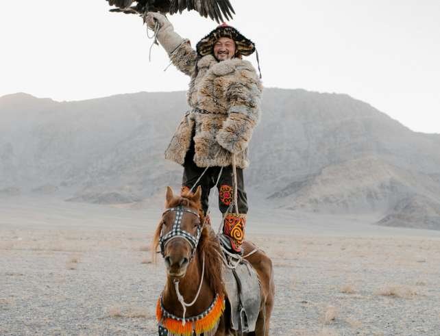 Mongolian hunter with eagle on horseback, showcasing cultural heritage and freedom.