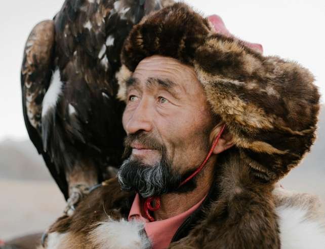 Portrait of a traditional eagle hunter with a majestic bird perched on his arm, showcasing cultural heritage.