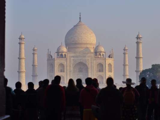 Silhouetted tourists admire the Taj Mahal's iconic beauty at sunrise, a UNESCO World Heritage site.