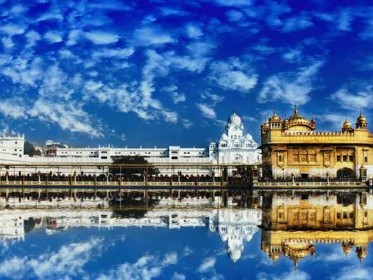 The Golden Temple, Harmandir Sahib, in Amritsar beautifully reflected in water with a vivid blue sky.