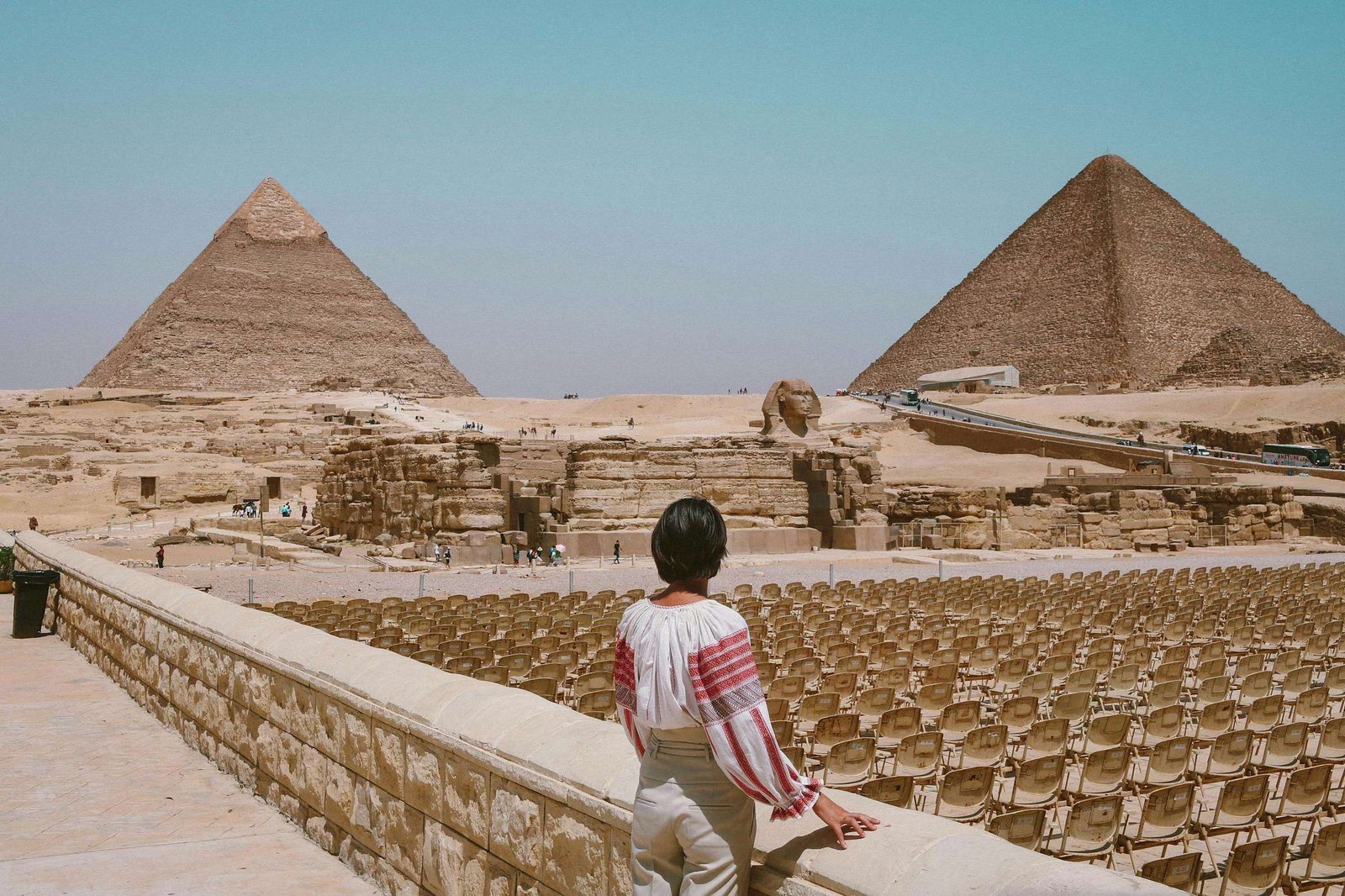 A tourist admires the Great Pyramids and Sphinx in Giza, Egypt under the clear daytime sky.